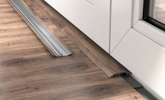 Wooden floor with a metal threshold leading to a white door.